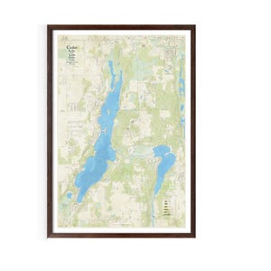 May include: A framed map of Cedar Lake and Little Cedar Lake in Minnesota. The map shows the lakes, surrounding land, and nearby roads. The map is printed in shades of green, blue, and brown.