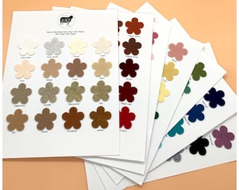 May include: A color chart of Merino wool blend felt in various shades, including pure white, silver white, ivory, wheat, fawn, sand, cappuccino, granite, yellowstone, hay, maple leaf, cherry, copper penny, auburn brown, brown, green, navy blue, blue, black, and amethyst. The felt is arranged in a fan shape, with each color represented by a small flower-shaped sample.