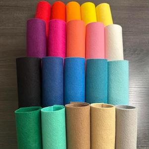 May include: A collection of colorful felt rolls in various shades, including red, orange, yellow, purple, pink, blue, green, brown, and white. The rolls are arranged in neat rows, showcasing the diverse color palette and textured surface of the felt.