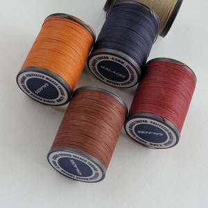 May include: Five spools of waxed thread in different colors: brown, orange, red, navy blue, and beige. Each spool has a label that reads "GALACES" and "0.5MM - CORED ROUND WAXED THREAD - POLYESTER".