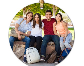 May include: Four friends, two men and two women, are sitting on a stone wall outdoors. They are all smiling and looking at the camera. They are wearing casual clothing and have backpacks with them.