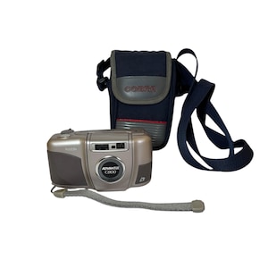 May include: A silver and gray Kodak Advantix C800 camera with a gray wrist strap and a black Cobra camera case with a shoulder strap. The camera case has a gray top and red stripe.