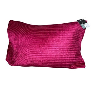 May include: A rectangular magenta velvet cushion with a stitched, curved design on the front. The cushion has a soft, plush appearance and a tag that reads "MALINI". Ideal for home decor.