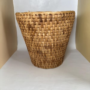 May include: A hand-woven basket with a flared design. The basket is constructed from natural-toned, closely woven fibres, giving it a textured appearance. The basket's design is simple and practical, suitable for storage or display.