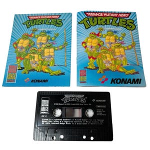 May include: Two Teenage Mutant Hero Turtles game boxes and a cassette tape. The boxes are blue with the Turtles characters and the word "Turtles". The cassette tape is black with the word "Turtles" and "Konami".
