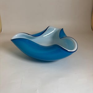 May include: A bowl made of glass with a vibrant blue exterior and a smooth, opaque white interior. The bowl features a distinct, organic, wavy rim design with three prominent points, creating a fluid and asymmetrical shape in its construction.
