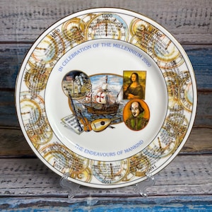 May include: A commemorative ceramic plate titled In Celebration of the Millennium 2000 The Endeavours of Mankind. The rim features a clock-like timeline from 1000 to 1900. The centre displays a sailing ship, the Mona Lisa, and William Shakespeare.