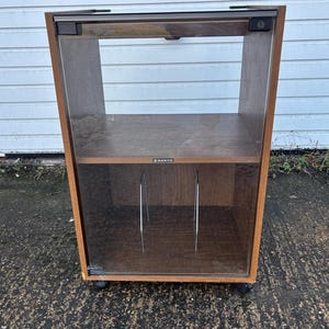 May include: A vintage wooden cabinet with a glass door and two shelves. The cabinet has a dark brown finish and is on castors. The word "SANYO" is visible on the front of the cabinet.