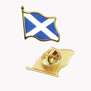May include: A gold-coloured metal pin badge in the shape of the Scottish flag, with a blue background and a white saltire. The pin has a gold border and a pin back. The second pin shows the back of the badge.