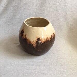 Op de afbeelding: Een ronde keramische pot met een bruine en witte glazuur. De pot heeft een brede opening en een afgeronde bodem.