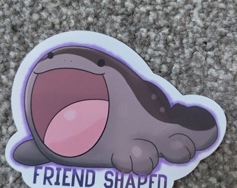 May include: A sticker featuring a cartoon character in shades of gray, pink, and purple. The character has a wide open mouth and the text "FRIEND SHAPED" in purple. The sticker has a white border.