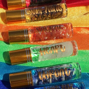 May include: Seven gold-capped glass roller bottles with different colored crystals and labels. The labels read "Crown", "Third Eye", "Throat", "Heart", "Sacral", "Solar Plexus", and "Root".