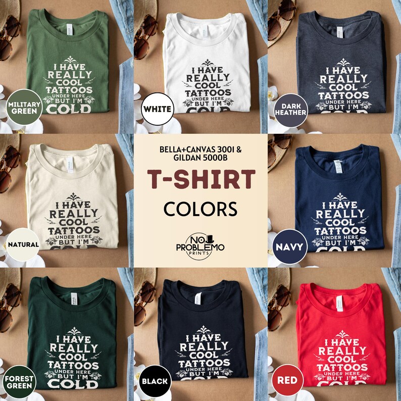 May include: A collection of eight short-sleeved crew neck t-shirts in military green, white, dark heather, natural, navy, forest green, black, and red. Each shirt features the black text I HAVE REALLY COOL TATTOOS UNDER HERE BUT I'M COLD.