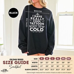 May include: A black crewneck sweatshirt featuring white text that reads I HAVE REALLY COOL TATTOOS UNDER HERE BUT I'M COLD. A size guide chart is included, listing widths from 20 to 30 inches, lengths from 27 to 32 inches, and sleeve lengths from 33.5 to 38.5 inches.