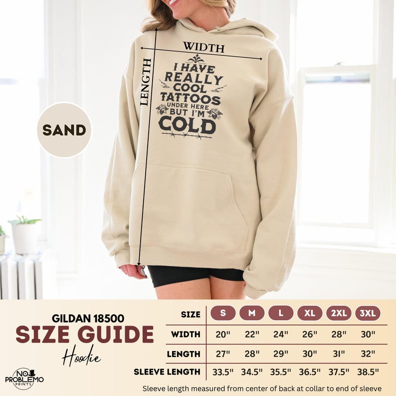 May include: A sand-colored hoodie featuring the black text I HAVE REALLY COOL TATTOOS UNDER HERE BUT I'M COLD. A size guide chart is included, listing widths from 20 to 30 inches, lengths from 27 to 32 inches, and sleeve lengths from 33.5 to 38.5 inches.