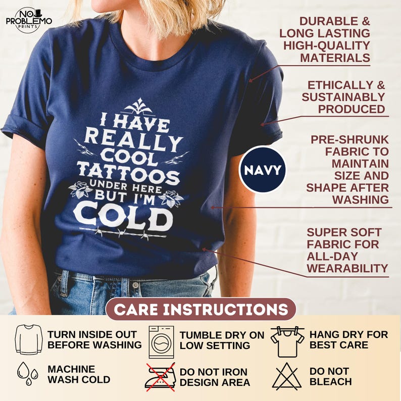 May include: A navy blue short-sleeved t-shirt featuring white text that reads I HAVE REALLY COOL TATTOOS UNDER HERE BUT I'M COLD. The shirt includes graphic details of roses and barbed wire. The image displays product features and care instructions.