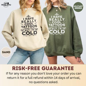 May include: Two crewneck sweatshirts, one in sand and one in military green, each featuring the black or white printed text: I HAVE REALLY COOL TATTOOS UNDER HERE BUT I'M COLD, accompanied by decorative floral and barbed wire graphic elements.