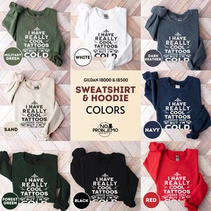 May include: A collection of Gildan 18000 and 18500 sweatshirts and hoodies in military green, white, dark heather, sand, navy, forest green, black, and red. Each garment features the white text I HAVE REALLY COOL TATTOOS UNDER HERE BUT I'M COLD.