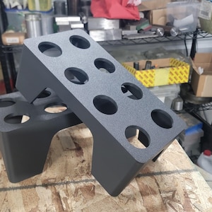 May include: Two dark gray, rectangular stands with multiple circular openings. The stands are made of a textured material and are designed to hold items. They are positioned on a wooden surface.