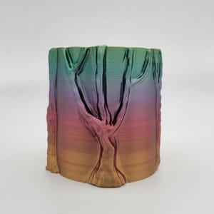 Puede incluir: Un jarrón de impresión 3D con colores de arcoíris y un diseño de árbol. El jarrón está hecho de un material liso, similar al plástico, y tiene un degradado de colores que va del verde al dorado.