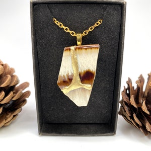 May include: A gold chain necklace with a brown and white ceramic pendant. The pendant has a gold accent in the shape of a tree.