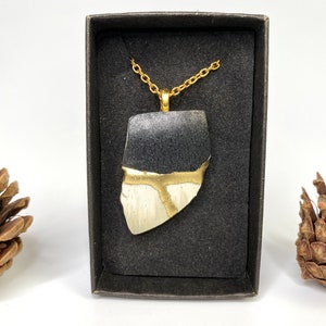 May include: A black and white ceramic pendant with gold accents hangs from a gold chain. The pendant is in a black box.