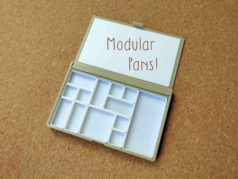 Pu&ograve; includere: Una tavolozza di plastica beige vuota con un coperchio bianco che dice "Modular Pans!" La tavolozza ha 12 pozzetti vuoti di diverse dimensioni.