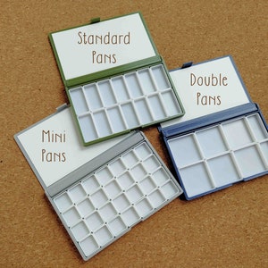 Pu&ograve; includere: Tre palette di colori ad acquerello con vaschette di diverse dimensioni. La palette superiore &egrave; verde e dice "Standard Pans". La palette centrale &egrave; grigia e dice "Mini Pans". La palette inferiore &egrave; blu e dice "Double Pans".