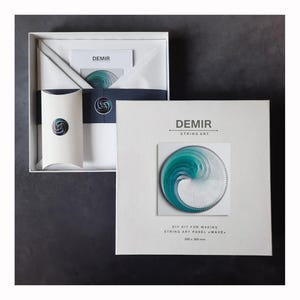 Pode incluir: Um conjunto de caixa branca contendo um kit de arte de cordas DIY. O kit inclui uma caixa branca com a marca "DEMIR" e um painel de arte de cordas concluído com um design de onda turquesa e branco. A caixa também contém instruções e outros materiais.
