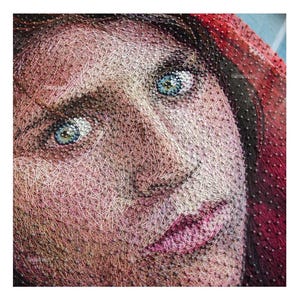 Può includere: Primo piano del viso di una donna, realizzato con filo, con occhi azzurri e un cappuccio rosso.