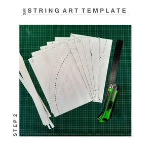 May include: A green cutting mat with a ruler, a craft knife, and several white paper templates labelled with numbers. The templates are for string art projects. The text "STEP 2" is written vertically on the left side of the image.