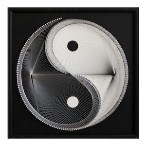 May include: A framed Yin and Yang string art piece. The artwork features a black square frame with a black background. The Yin and Yang symbol is created with white string, with a black dot in each half. The string art is a minimalist design.