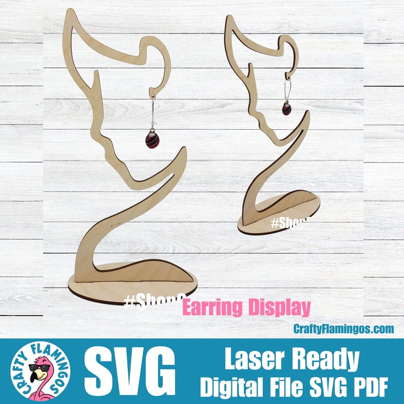 May include: Wooden earring display stand with a silhouette of a person's head and neck. The stand is laser cut and ready to be assembled. The stand is shown with a pair of earrings on it.