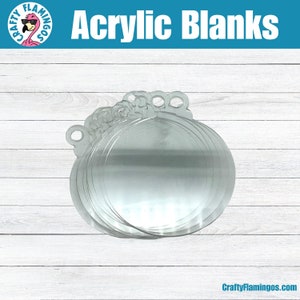 May include: A stack of clear acrylic ornament blanks with a hole for hanging. The image has the text "Acrylic Blanks" in white on a blue background. The logo for Crafty Flamingos is in the upper left corner and the website is in the lower right corner.
