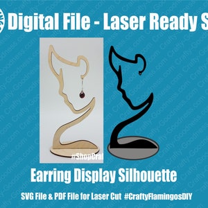 May include: A laser-cut wooden earring display stand in the shape of a woman's profile. The stand is brown and has a small round base. The text "#Shoperal" is printed on the base. The stand is shown next to a black silhouette of the same design.