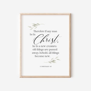 May include: A printable wall art print with a white background and black text. The text reads "Therefore if any man be in Christ, he is a new creature: old things are passed away; behold, all things become new. 2 Corinthians 5:17". The text is in a cursive font and is surrounded by green leaves.