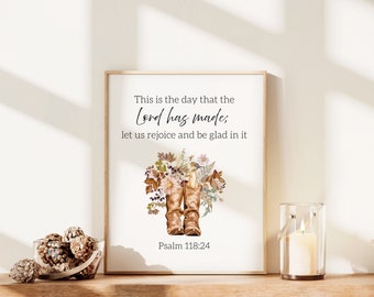 May include: Framed art print featuring the text "This is the day that the Lord has made; let us rejoice and be glad in it" and "Psalm 118:24". The artwork includes watercolor illustrations of cowboy boots and floral arrangements. The frame is a light brown color.