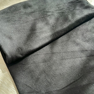 May include: A black fabric folded in half. The fabric has a smooth texture and a slight sheen.