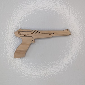 May include: A wooden replica of the Nintendo Zapper gun. The gun is light brown and has a black Nintendo Zapper logo on the side.