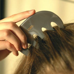 Puede incluir: Un peine para el cabello de pl&aacute;stico gris con tres p&uacute;as. El peine tiene la palabra "cure." impresa en letras doradas.
