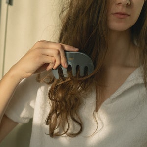 Puede incluir: Una persona con cabello largo y casta&ntilde;o est&aacute; usando un peine gris con la palabra "cure." impresa en &eacute;l para peinarse.