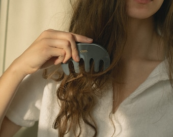 May include: A person with long brown hair is using a grey comb with the word "cure." printed on it to style their hair.