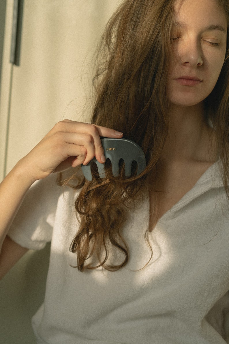 Puede incluir: Una persona con cabello largo y casta&ntilde;o est&aacute; usando un peine gris con la palabra "cure." impresa en &eacute;l para peinarse.
