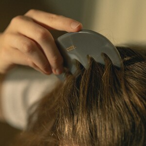 Puede incluir: Un peine para el cabello de pl&aacute;stico gris con tres p&uacute;as y la palabra "cure." impresa en &eacute;l. El peine se est&aacute; utilizando para peinar el cabello de una persona.