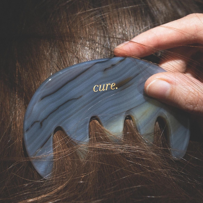 Puede incluir: Un peine de &aacute;gata azul y blanco con la palabra "cure." inscrita en &eacute;l. El peine se est&aacute; utilizando para cepillar el cabello casta&ntilde;o de una persona.