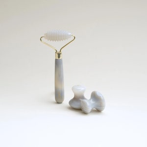 May include: A set of two grey agate facial rollers. One roller is a face roller with a handle and the other is a double-ended face roller.