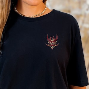 May include: Black t-shirt with a red and gold graphic of a stylized face on the left chest.