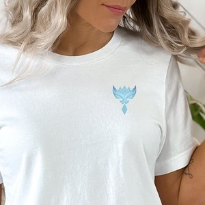 May include: White t-shirt with a blue abstract design on the front. The design is a stylized bird with a diamond shape in the center.