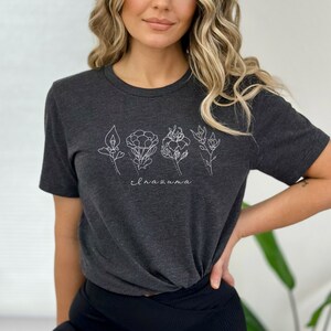 May include: A dark gray t-shirt with a white outline of five different flowers and the word "elnazuna" printed on the front.