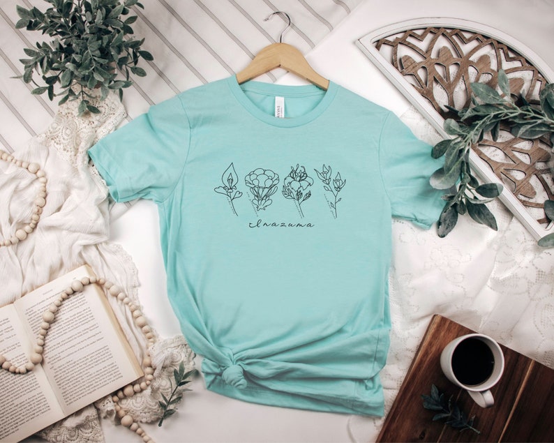 May include: A light blue t-shirt with a graphic of stylized flowers and the text "el nazareno".
